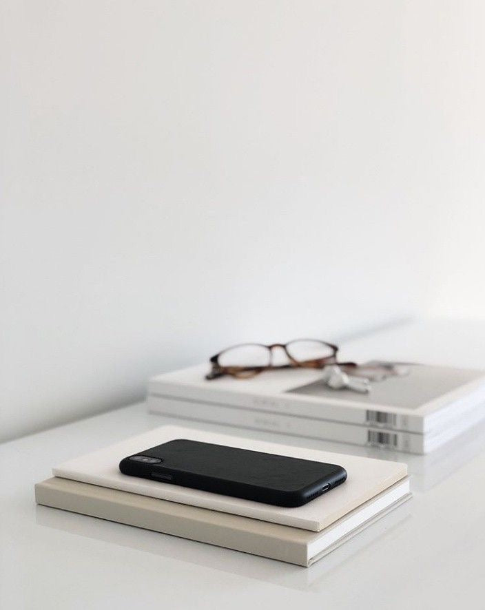 Smartphone resting on stacked books on a minimalist desk, representing ongoing voice note coaching support and personal guidance.