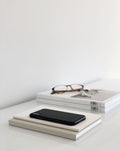 Smartphone resting on stacked books on a minimalist desk, representing ongoing voice note coaching support and personal guidance.