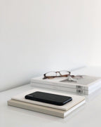 Smartphone resting on stacked books on a minimalist desk, representing ongoing voice note coaching support and personal guidance.